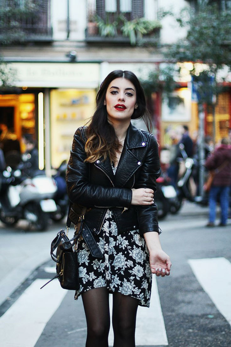 A woman wears a spring floral dress layered for warmth with a leather jacket and tights