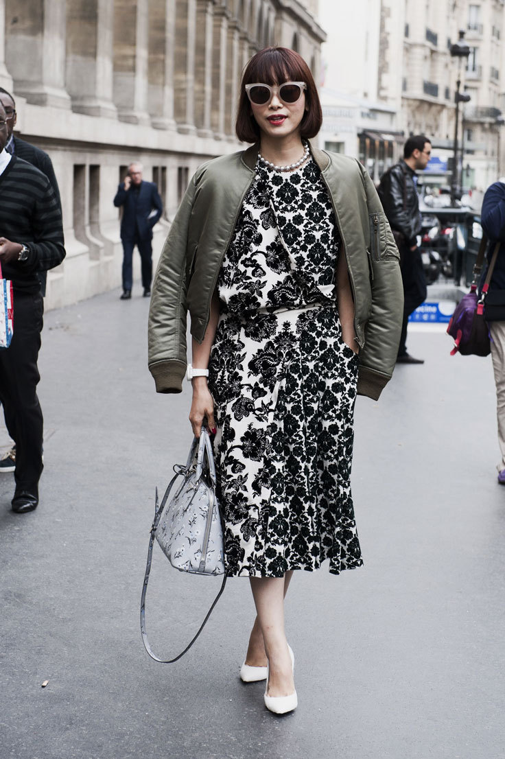 A woman wears a black and white floral dress layered with a green bomber jacket
