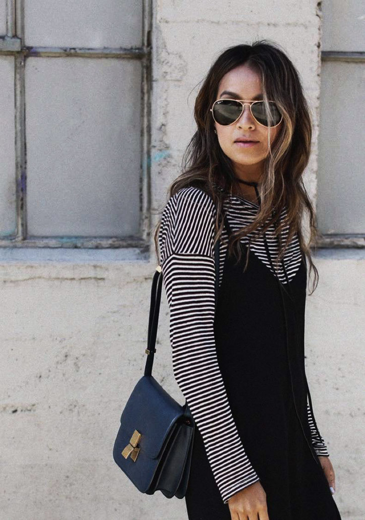 A woman wears sunglasses and a cute floral dress with a striped top underneath